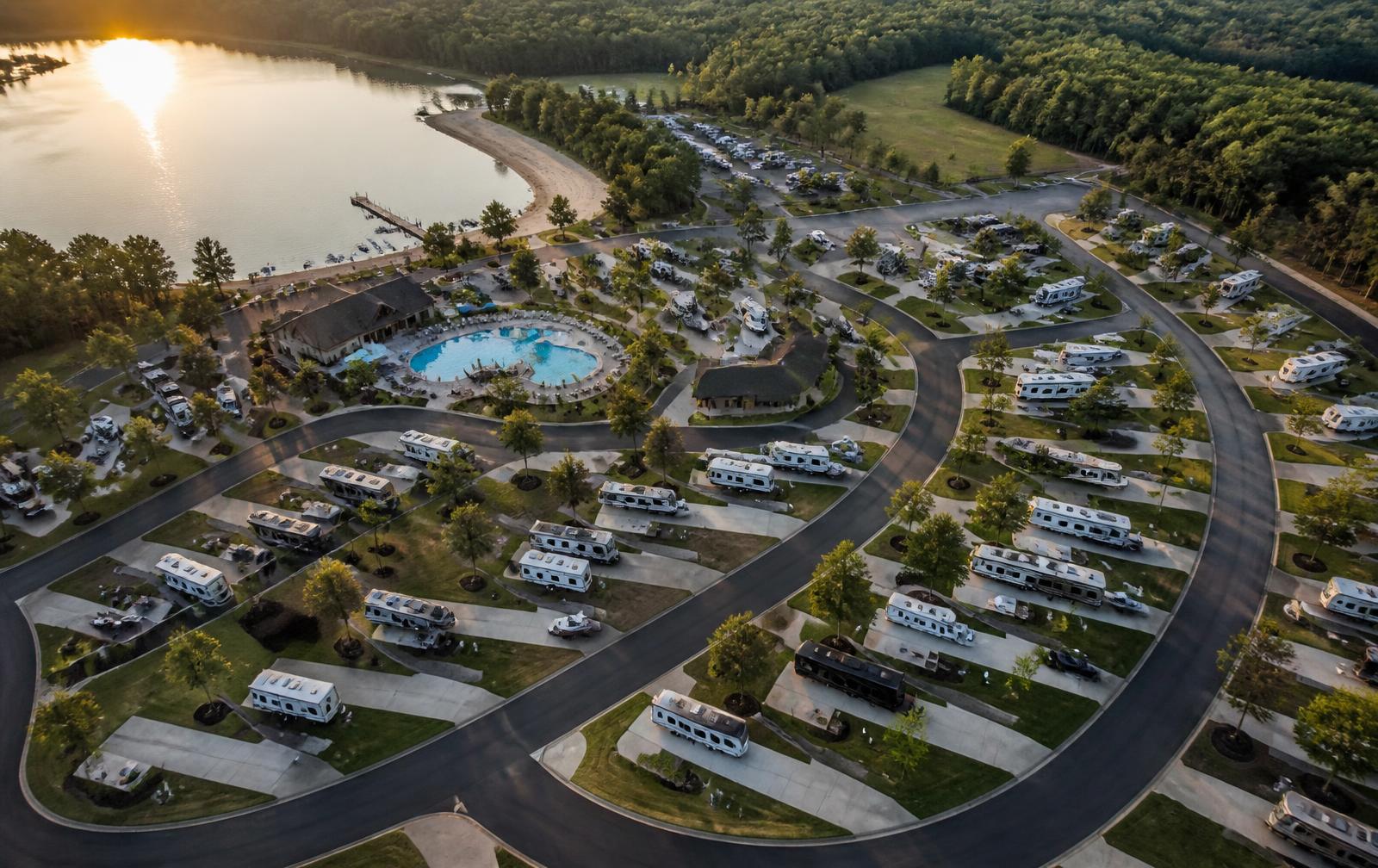 Aerial view of a lakeside RV resort with pool, clubhouse, beach and pull-through sites at golden hour