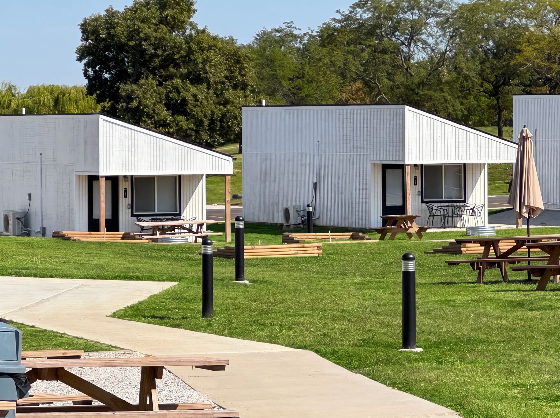 Row of white park-model cabins with picnic tables, patio seating and pathways at a campground resort
